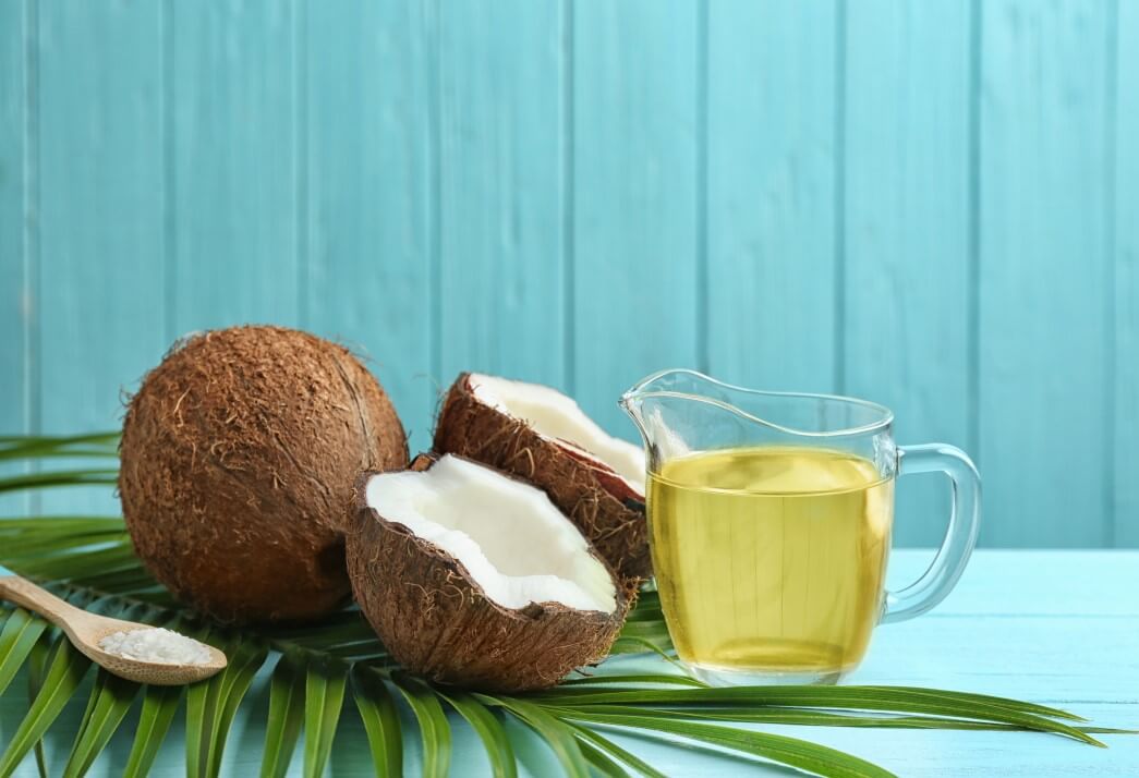A whole coconut, halved coconut and a measuring cup of coconut oil sitting on top of a counter waiting to be used in a hair care routine