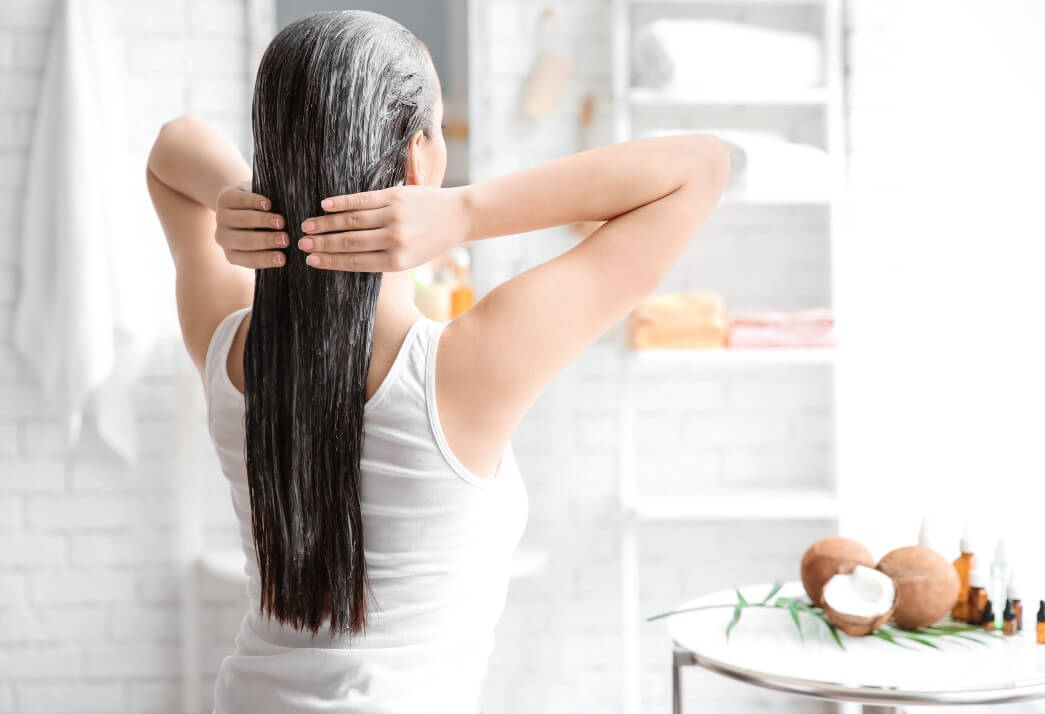 A woman applying Coconut Oil in her long black hair to promote a healthy hair care routine