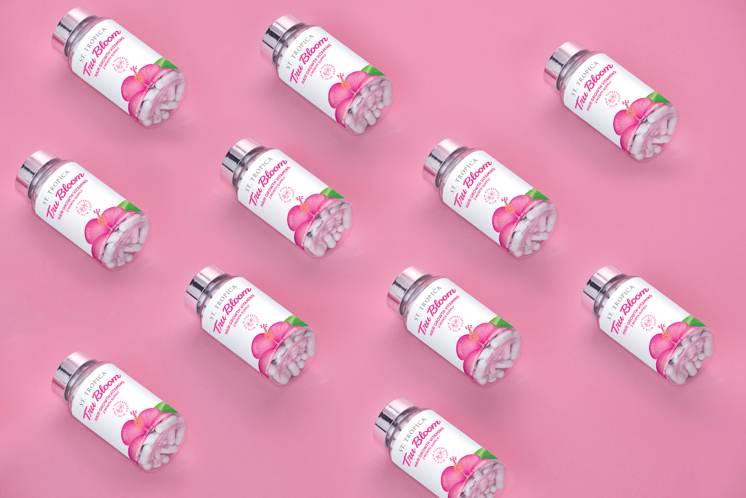 ST. TROPICA Tru Bloom Vitamin bottles laying on their side on a pink background. 