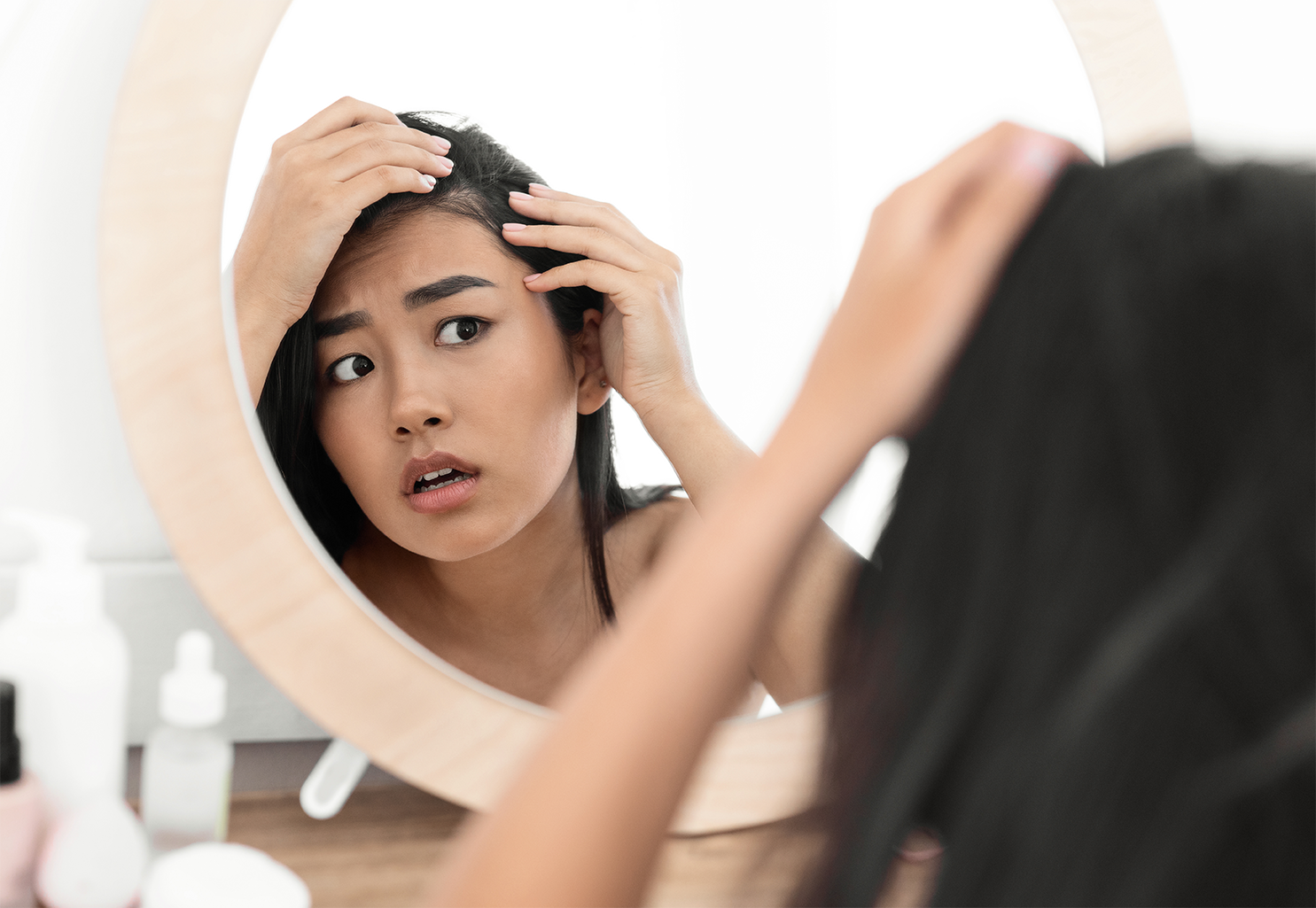 Woman looking at herself in the mirror concerned over hair thinning above her temple. 