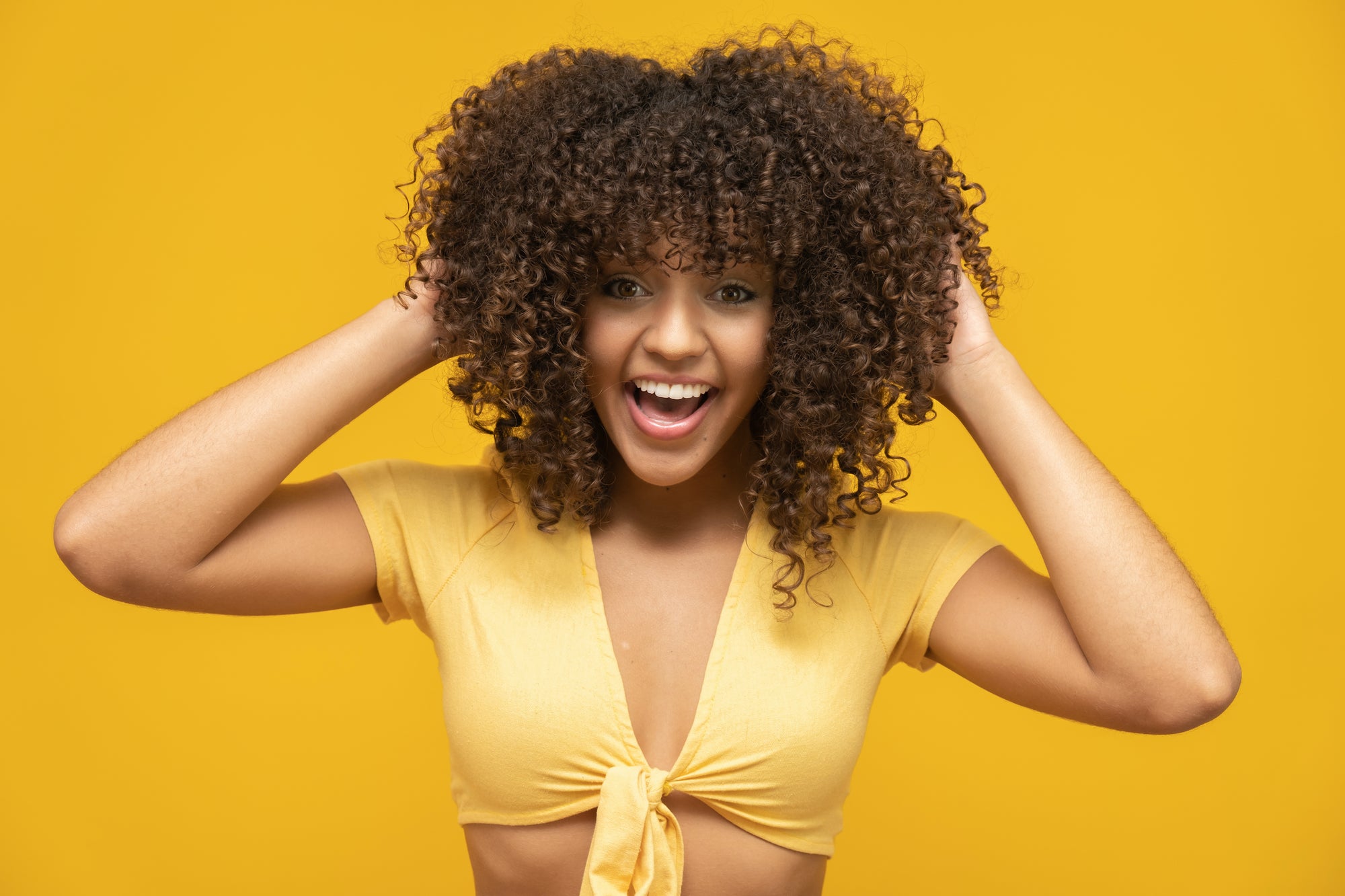 Woman with tight curls in yellow top touches hair
