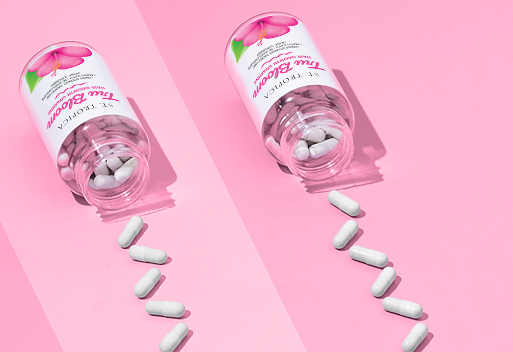 Tru Bloom Vitamin bottles on pink surface with vitamins in front of bottle in a line