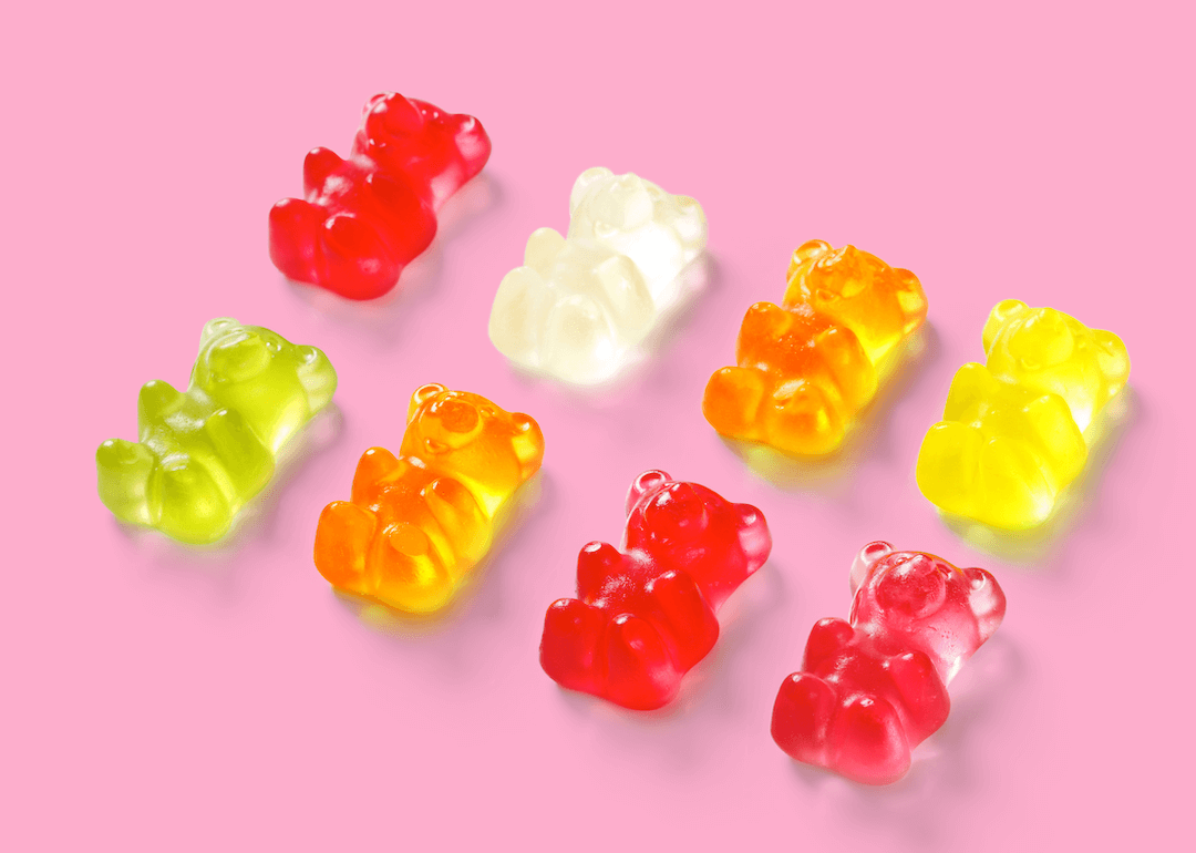 Brightly colored gummy bears placed in two lines on a pink background. 