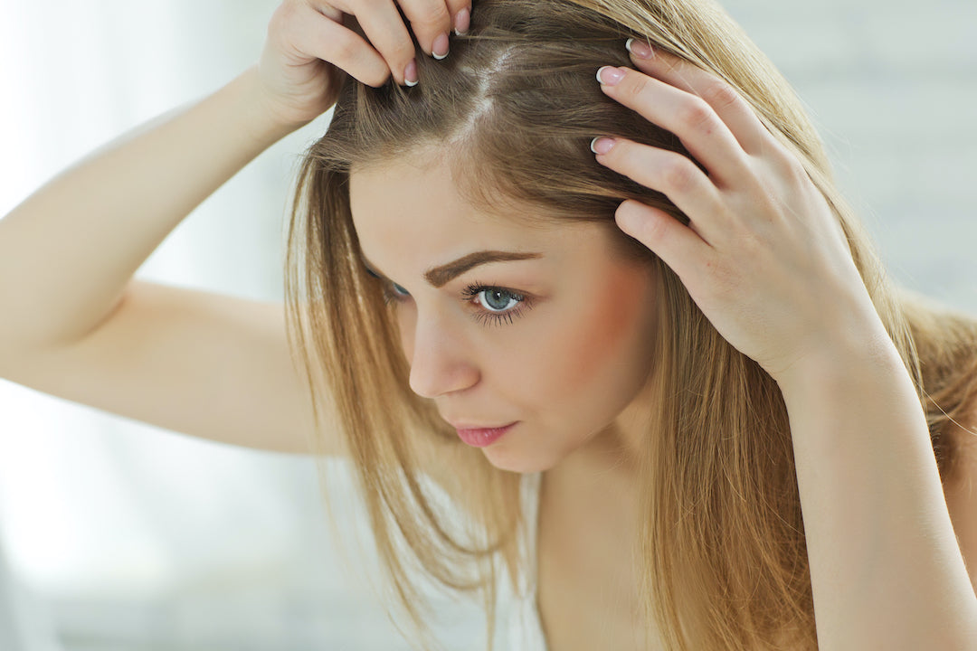 Blonde woman looking at her scalp in the mirror with concern.